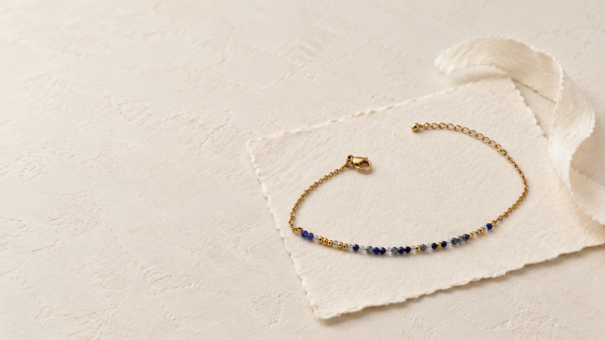 Bracelet à message en code Morse, en pierres naturelles bleues et acier inoxydable doré, posé sur une carte écrue.